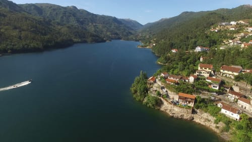 Vista aérea do Remote Care & Co aninhado na costa lacustre montanhosa de Braga com águas azuis e colinas florestadas