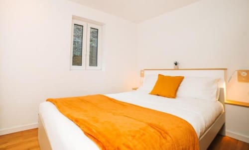 Quarto luminoso na villa Casa Colina em Salamonde com roupa de cama laranja, lençóis brancos e janela com vista para a montanha
