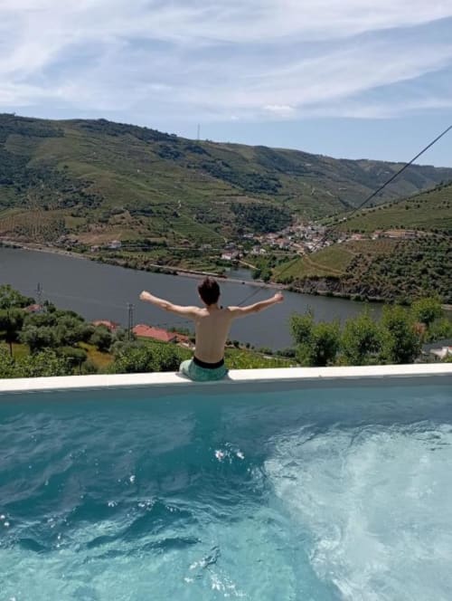 Homem sem camisa com os braços levantados em piscina azul-turquesa com vista do vale do rio Douro em Tomás Barqueiro, Folgosa