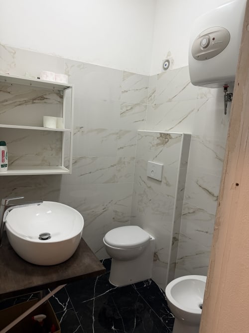 Bagno moderno nell'appartamento Zappy Domus con pareti in marmo, lavabo rotondo bianco, wc, bidet e scaldabagno a parete