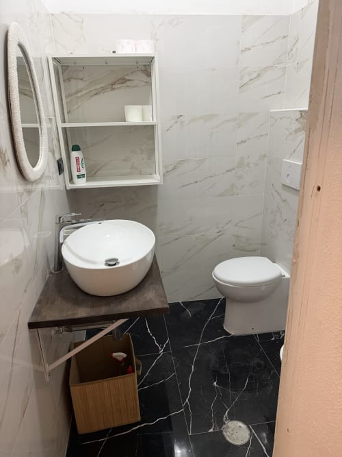 Bagno moderno nell'appartamento Zappy Domus con lavabo rotondo, wc, piastrelle effetto marmo e pavimento scuro a Castellaneta
