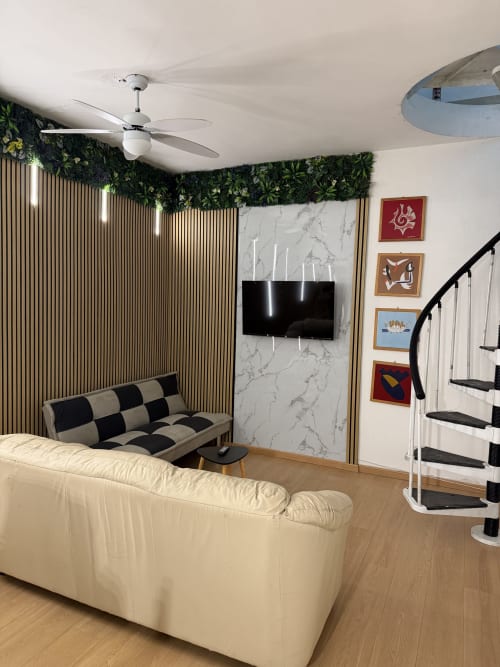 Elegante soggiorno con divano color crema, poltrona beige e nera, TV a parete, pannelli rigati e piante verdi