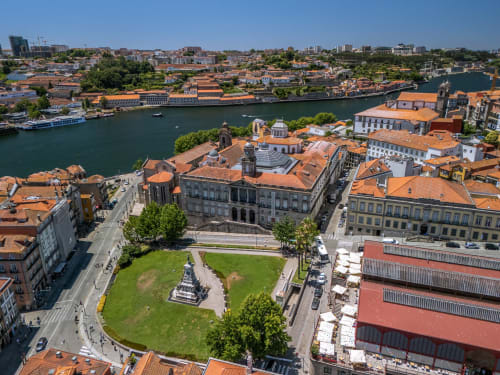 Vista aérea do bairro histórico ribeirinho do Porto com edifícios de telhados laranja, praça verde e rio Douro na AgapeStay