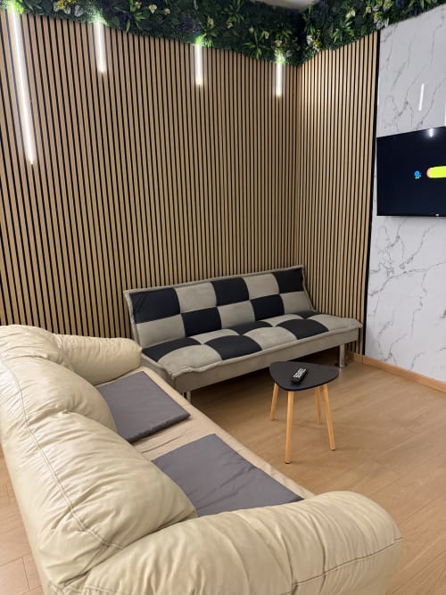 Moderno soggiorno presso Zappy Domus con divano a L beige, divano a scacchi bianco e nero, parete in doghe di legno e TV a parete