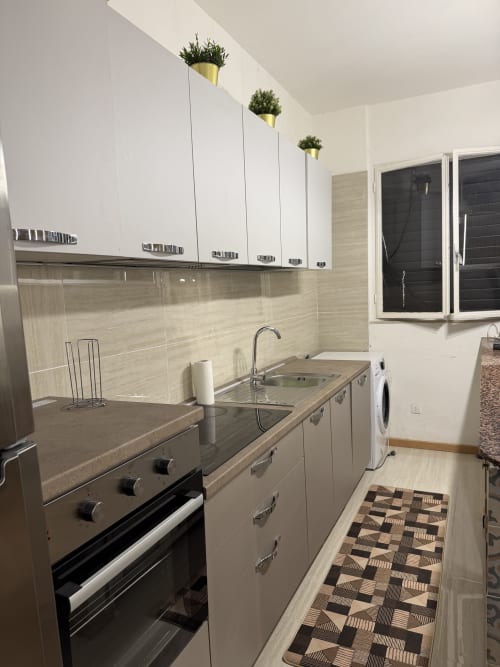 Cucina moderna con mobili bianchi, rivestimento beige, elettrodomestici in acciaio inox e tappeto geometrico a Zappy Domus