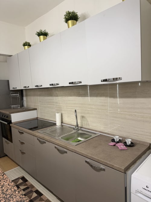 Cucina moderna in appartamento a Castellaneta Marina con mobili bianchi, rivestimento beige e lavello in acciaio inossidabile