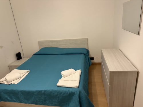 Camera da letto in appartamento B&B a Castellaneta Marina con copriletto blu, mobili in legno chiaro e cuscini bianchi