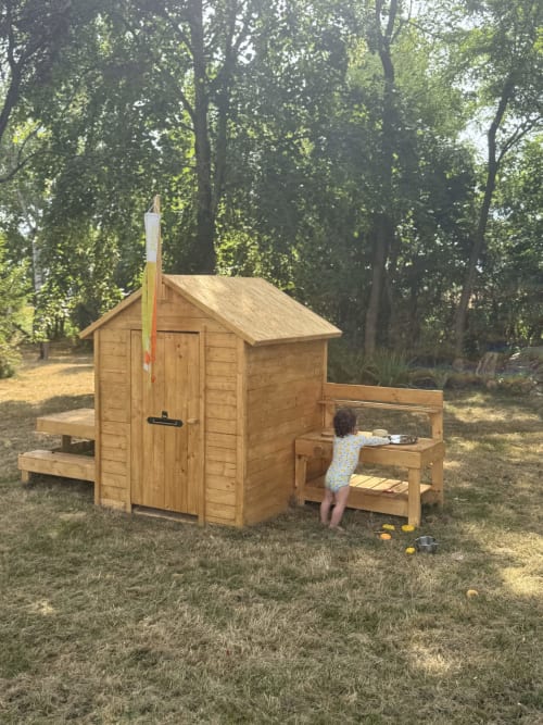 Enfant jouant dans une maisonnette en bois avec banc, dans le jardin de Saint-Pierre-des-Ormes à Maisons Noisette