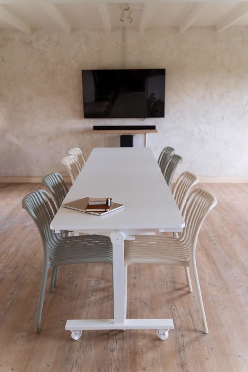 Salle de conférence moderne aux Maisons Noisette avec table blanche, chaises argentées, écran TV et parquet