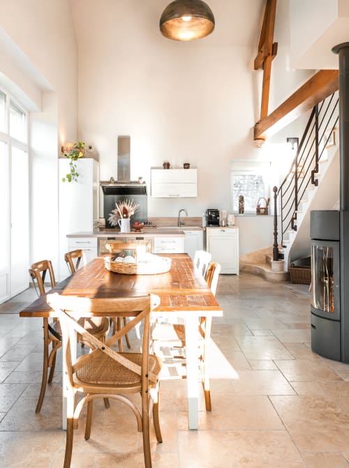 Cuisine-salle à manger lumineuse et spacieuse du gîte Le Hameau de Céline avec table en bois, placards blancs et escalier.