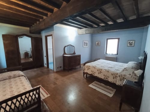 Spacious bedroom at Agriturismo Aggazzotti with twin beds, wooden beams, blue walls, and period furniture