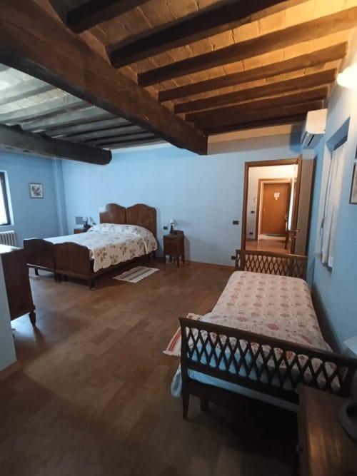 Spacious bedroom at Agriturismo Aggazzotti with wooden beams, two beds, light blue walls, and rustic furnishings