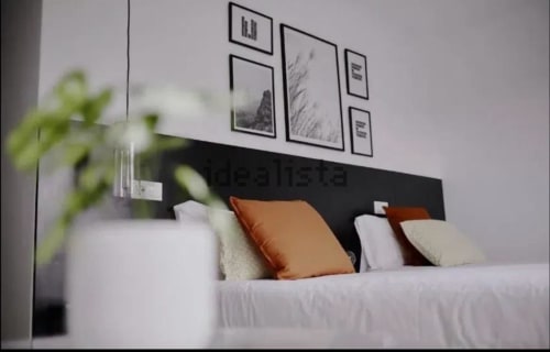 Dormitorio moderno en Hostel Zarey en Perillo con cama blanca, almohada naranja, cabecero negro y arte mural enmarcado