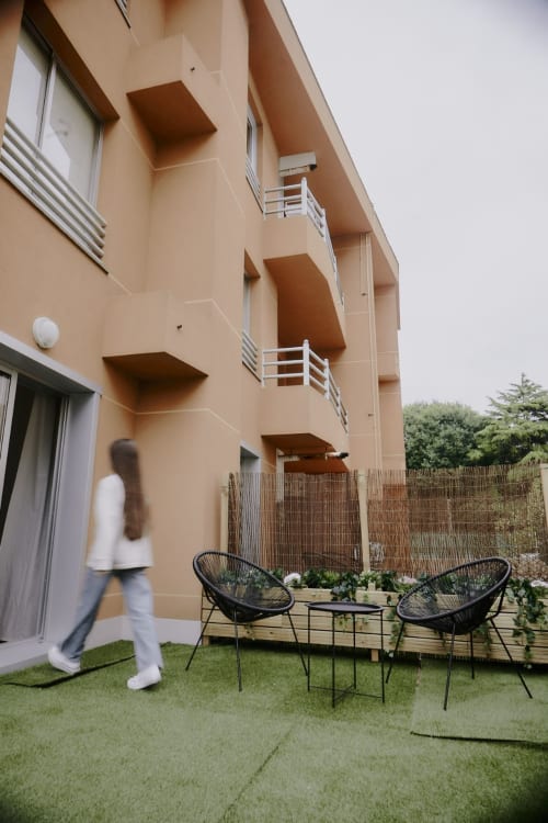 Terraza moderna del Hostel Zarey en Perillo con sillas negras, césped verde y fachada color melocotón