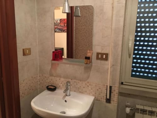 Bagno moderno presso la Domum Vaticani Rome B&B con lavabo bianco, specchio, piastrelle e scaffale con accessori
