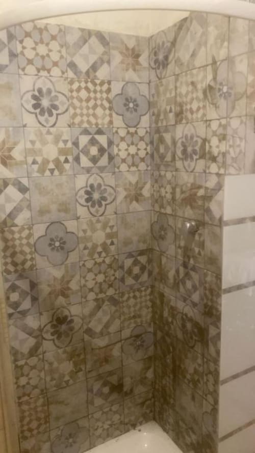 Nicchia doccia rivestita in piastrelle decorative con motivi geometrici e floreali nel bagno di una struttura ricettiva romana