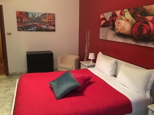 Camera matrimoniale moderna all'hotel Domum Vaticani Roma con letto rosso, cuscini bianchi e quadri con rose su parete accent bordeaux