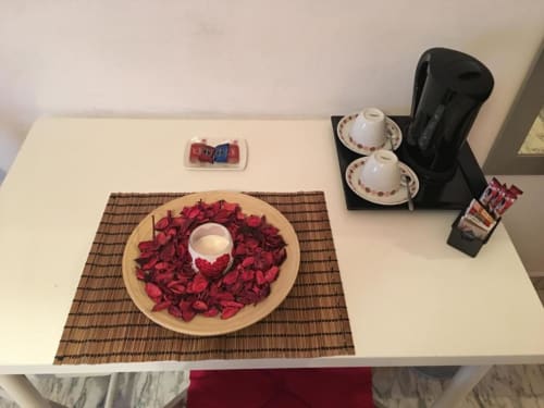 Allestimento benvenuto presso la Domum Vaticani B&B di Roma con petali di rosa, servizio di tè e articoli da toeletta freschi su una scrivania bianca.