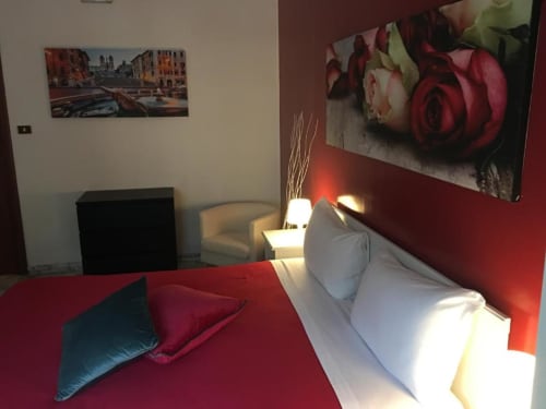Moderna camera matrimoniale a Domum Vaticani Roma con parete rossa, biancheria bianca, quadri di rose e veduta della città