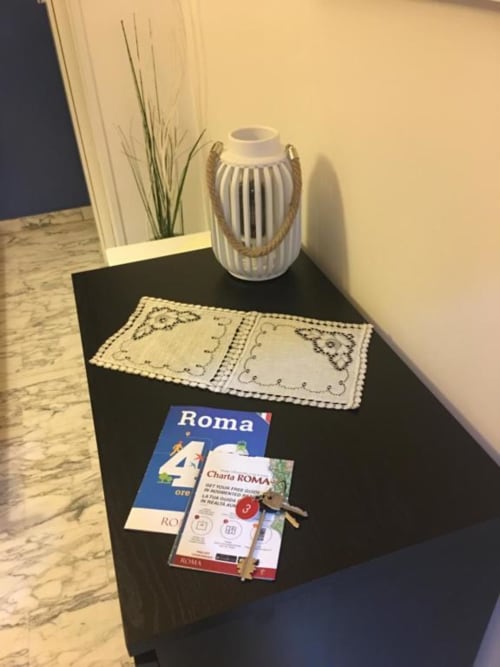 Scrivania nera nella stanza Domum Vaticani Roma con guide di viaggio, placemat decorativo, vaso lanterna bianco e pianta verde
