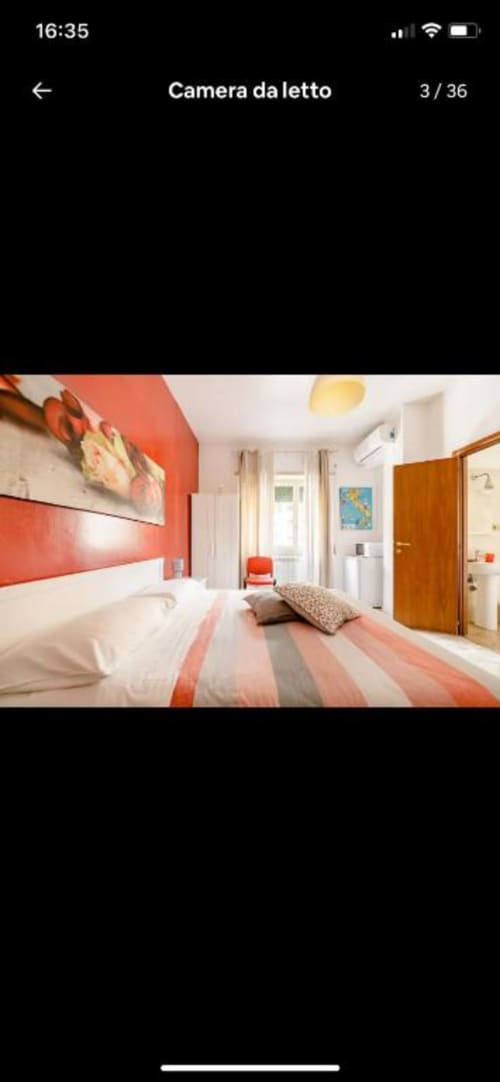 Camera da letto moderna e doppia a Domum Vaticani Roma con parete color corallo, biancheria bianca, porta in legno e luce naturale abbondante