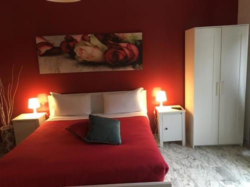 Camera da letto moderna presso Domum Vaticani Roma con pareti rosse, comodini bianchi, illuminazione calda e pavimenti in marmo