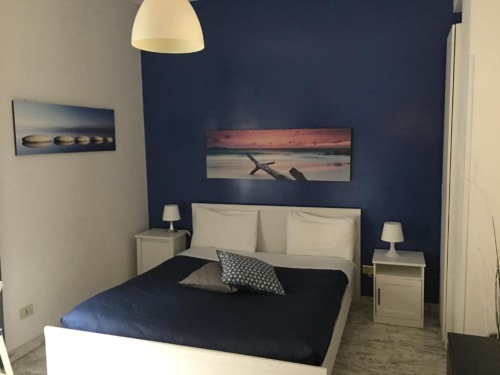 Camera da letto moderna a Domum Vaticani Roma con parete blu navy, letto bianco, quadri costieri e lampade comodino.