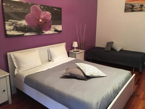 Camera tripla moderna presso Domum Vaticani B&B Roma con parete accentata viola, letto bianco e quadri con orchidee