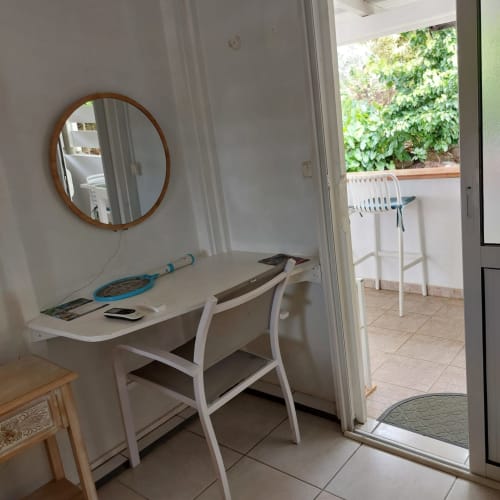 Bureau moderne avec miroir rond et chaise dans une chambre lumineuse du bungalow Coco Guadeloupe aux Saintes, vue sur le jardin et terrasse