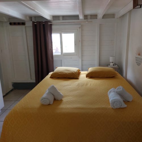 Chambre ensoleillée du bungalow Coco Guadeloupe avec couverture jaune, serviettes et portes vue sur mer aux Saintes