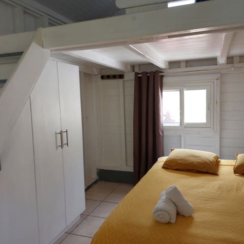 Chambre de bungalow à Coco Guadeloupe avec linge de lit jaune, armoire blanche et portes donnant sur la mer aux Saintes