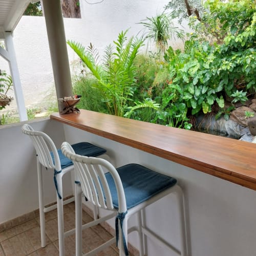 Véranda couverte avec comptoir en bois, chaises blanches et vue sur le jardin luxuriant du bungalow Coco Guadeloupe à Terre de Haut