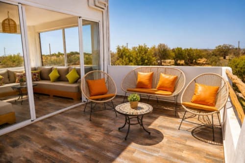 Terrasse de la Villa Castellum avec chaises tissées, coussins orangés et vue panoramique sur la campagne française