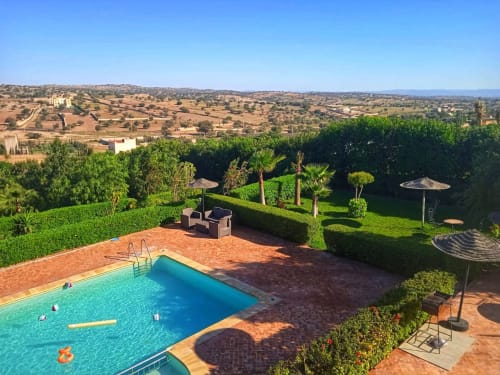 Piscine du Villa Castellum B&B avec vue sur la campagne marocaine, espace détente et jardins aménagés sous un ciel bleu dégagé