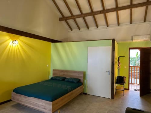 Chambre moderne à Caress'antillaise à Deshaies avec lit en bois, parure teal, murs jaune et vert, plafond à poutres