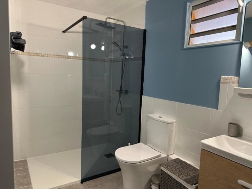 Salle de bain moderne avec douche à cadre noir, toilettes blanches, lavabo et murs bleu-blanc à l'hôtel Caress'antillaise à Deshaies