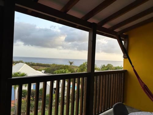 Terrasse face à l'océan de Caress'antillaise à Deshaies avec vue mer et montagnes, balustrade en bois et murs jaunes.