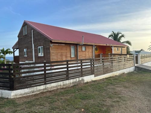 Appartement Caress'antillaise à Deshaies avec toiture rouge, façade bois, patio clôturé et vue montagne en Guadeloupe