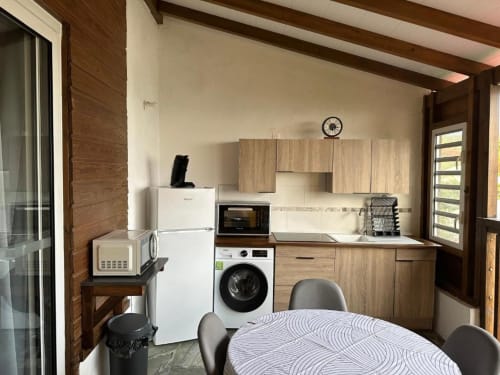 Cuisine moderne et coin repas dans l'appartement Caress'antillaise à Deshaies, avec électroménagers inox et vue sur les montagnes.