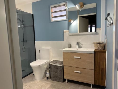Salle de bains moderne à Caress'antillaise avec murs bleu et blanc, meuble-lavabo en bois, toilettes blanches et douche vitrée
