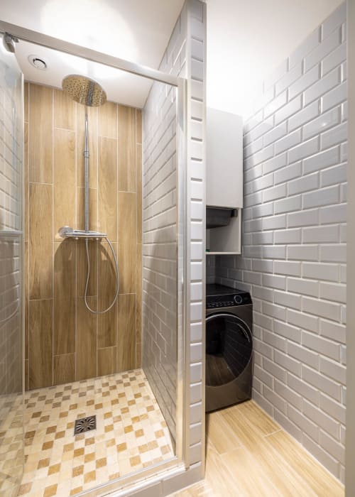 Salle de bain moderne avec douche pluie, carrelage imitation bois, mur en briques blanches et lave-linge dans un appartement à Épernay