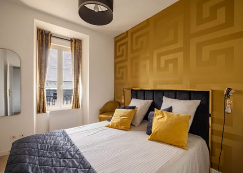Chambre luxueuse aux Secrets de Chef de Cave à Épernay avec mur d'accent doré, tête de lit noire et vue sur la ville