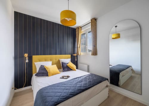 Chambre moderne au Secrets de Chef de Cave à Épernay avec tête de lit jaune, mur d'accent bleu marine et suspension ronde