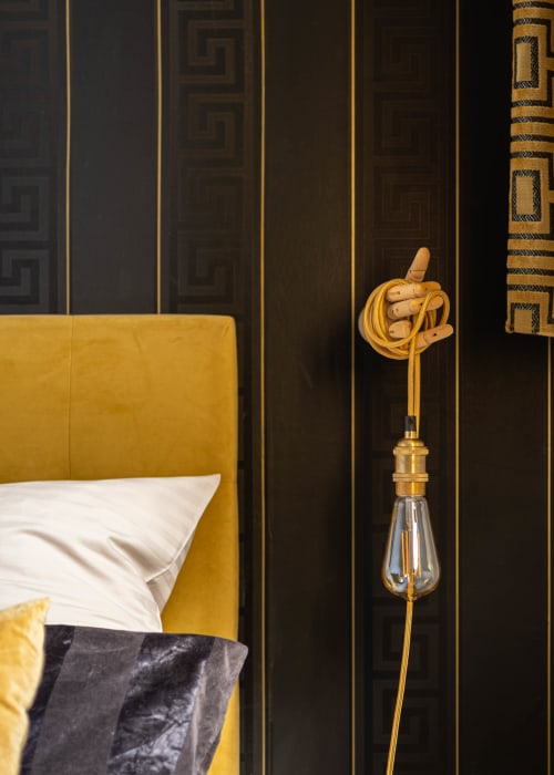 Chambre luxueuse à Épernay avec tête de lit moutarde, oreillers blancs et applique murale en laiton avec main en bois