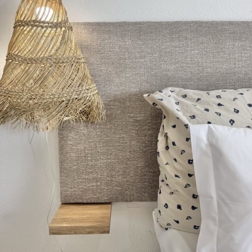 Detalle acogedor de dormitorio en Republica do Sul con lámpara colgante tejida, cabecero beige y ropa de cama estampada en Caparica.