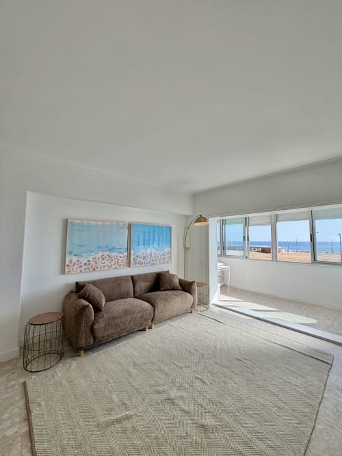 Luminosa sala de estar con vistas al mar, sofá marrón y arte de playa en Republica do Sul, Caparica