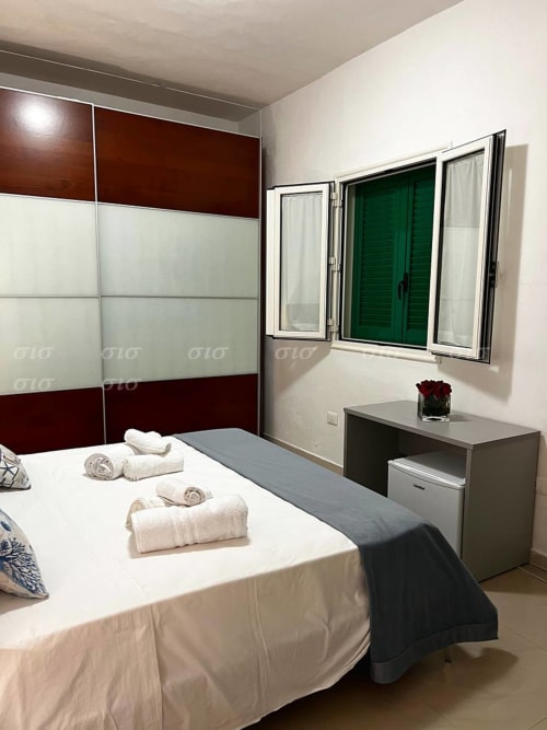 Camera da letto moderna alla villa Puglia Estate con armadio bordeaux e bianco, biancheria bianca, scrivania e finestra con persiane verdi