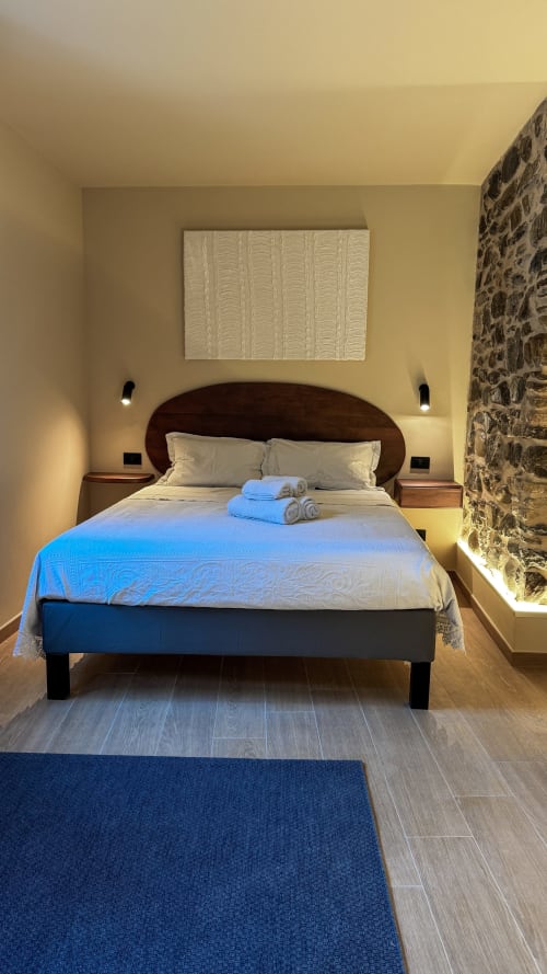 Camera accogliente del Talking Stones B&B a Dolceacqua con testata in legno scuro, biancheria beige, muro in pietra e moquette blu