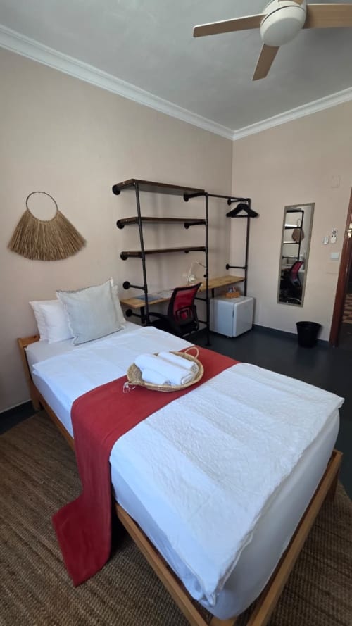 Ostro room at Casa de Océano hotel in Tarifa featuring bed with red runner, metal clothing rack, desk, and ceiling fan