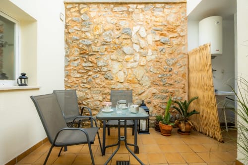 Terraza de patio con muros de piedra, mesa de comedor, sillas, plantas en macetas y biombo de madera en Apartamento Jaume B, Artà